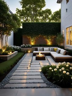 an outdoor living area with white flowers and lights on the side of the building, surrounded by greenery