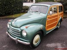 an old green car with wood trim parked in a parking lot next to some bushes