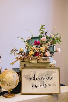 an adventure awaits sign sitting on top of a table next to a globe and flowers