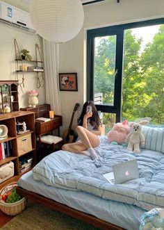 a woman sitting on a bed with a laptop in front of her, looking out the window