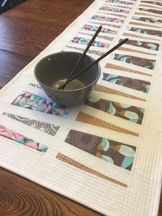 a bowl and two chopsticks sitting on top of a quilted table runner