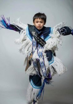 a young boy is dressed in blue and white clothing with feathers on his arms while dancing