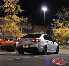 a white car is parked in the parking lot at night with its lights turned on