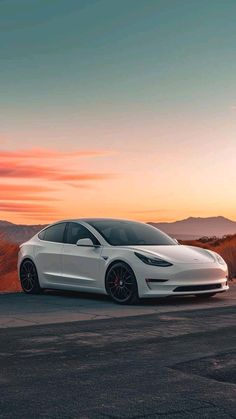 a white tesla model 3 parked on the side of a road at sunset with mountains in the background