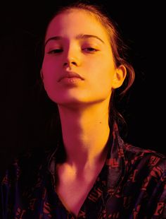 a woman with her eyes closed in front of a black background, wearing a patterned shirt