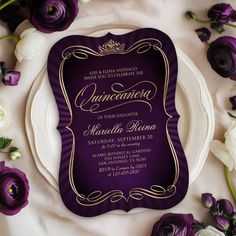 a purple and gold wedding card on a white plate surrounded by flowers, with the word quinceause written in cursive