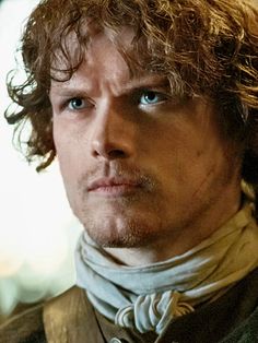 a close up of a person with long hair and blue eyes wearing a scarf around his neck