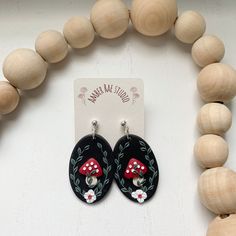 a pair of black and red earrings with white flowers on them next to a wooden bead necklace