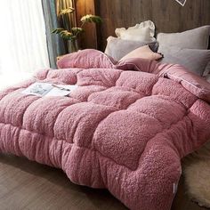 a bed with pink comforter and pillows on top of it in a room next to a window