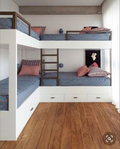 two bunk beds in a room with wooden floors and white walls, one is blue and the other has pink pillows