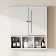 a white cabinet with three bottles and soaps in it on the wall next to a toilet