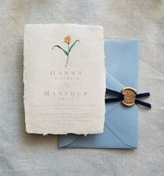 a wedding card with a wax stamp on it next to an envelope that has a flower