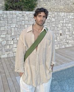 a man standing in front of a swimming pool wearing white pants and a green tie