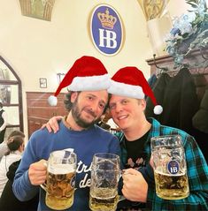 two men in santa hats are holding beer glasses and posing for the camera with their arms around each other