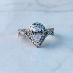 an engagement ring with a pear shaped diamond surrounded by pave diamonds on a marble surface