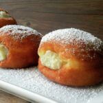 three doughnuts on a white plate with powdered sugar