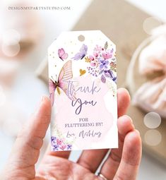 a hand holding a thank you tag with flowers and butterflies on it in front of a cupcake