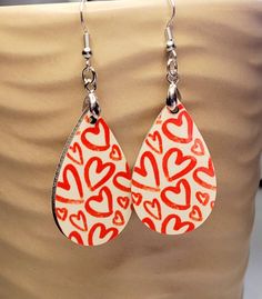 red and white heart shaped earrings hanging from a tan vase with silver hooks on it