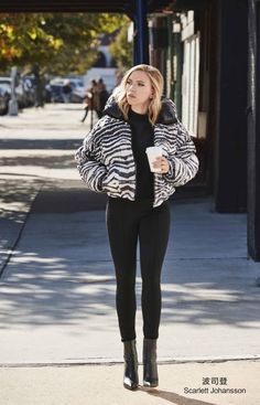 a woman is walking down the sidewalk while holding a coffee in her hand and looking off into the distance