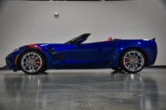 a blue sports car is parked in a large room with white walls and flooring