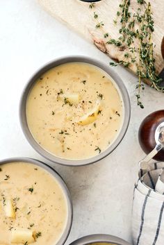 three bowls filled with soup and garnished with herbs next to a wooden spoon