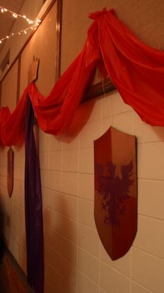 two red and purple banners hanging on the wall next to a white brick wall with lights strung from it