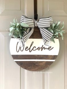 a welcome sign hanging on a door with greenery in the center and ribbon around it