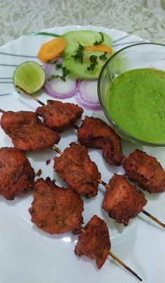 several skewers of food on a plate next to a bowl of green liquid