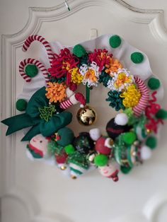 a christmas wreath hanging on the front door with ornaments around it and bells in the middle