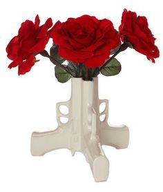 three red roses in a white vase on a stand with leaves and stems, isolated against a white background