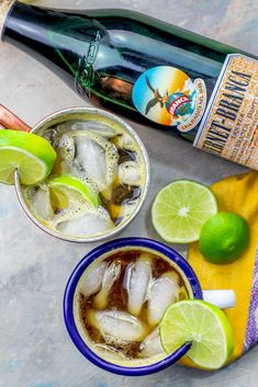 two glasses filled with ice and limes next to a bottle