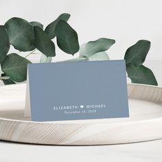 a place card sitting on top of a white plate next to a green leafy plant