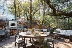 an outdoor dining area with wood flooring and stone fireplace in the background, surrounded by trees