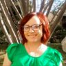 a woman with red hair and glasses standing in front of trees