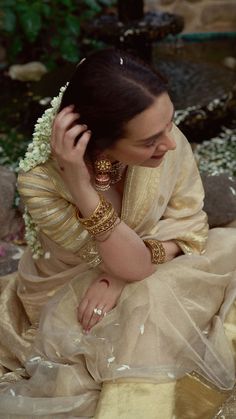 a woman sitting on top of a rock next to a river wearing gold bracelets