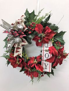 a christmas wreath with poinsettis and greenery hangs on the wall next to a sign that says joy