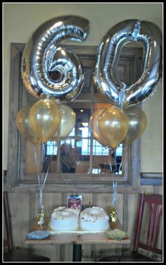 the table is set with two cakes and balloons in the shape of the number sixty