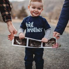 a little boy holding two photos with his parents'hands while walking down the road