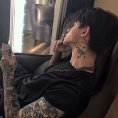 a man sitting in a chair with tattoos on his arms and legs, looking out the window