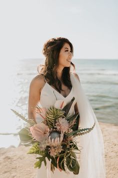 a woman standing on top of a beach holding a bouquet