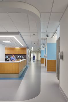 an empty hospital hallway with blue and yellow accents on the walls, people sitting at their desks