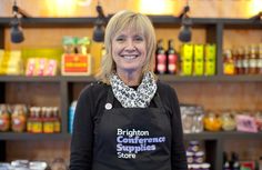 a woman wearing an apron standing in front of a store shelf filled with condiments