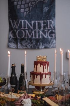 a table topped with a cake covered in icing next to wine bottles and candles