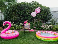 an inflatable pool and flamingo floaters are on the lawn near some bushes