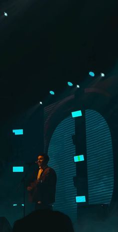 a man standing in front of a microphone on top of a stage with lights behind him