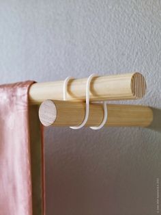 a pair of wooden clothes hangers on a pink curtain rod with two white straps