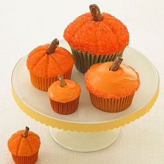 three cupcakes with orange frosting on a white plate and two small pumpkins