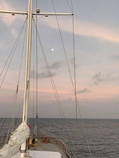 the sun is setting over the ocean on a sailboat in the distance, as seen from across the water