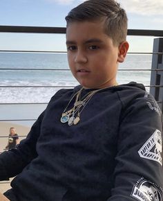 a young boy sitting on top of a bench next to the ocean