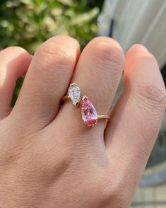 a woman's hand holding an engagement ring with two pear shaped pink and white diamonds